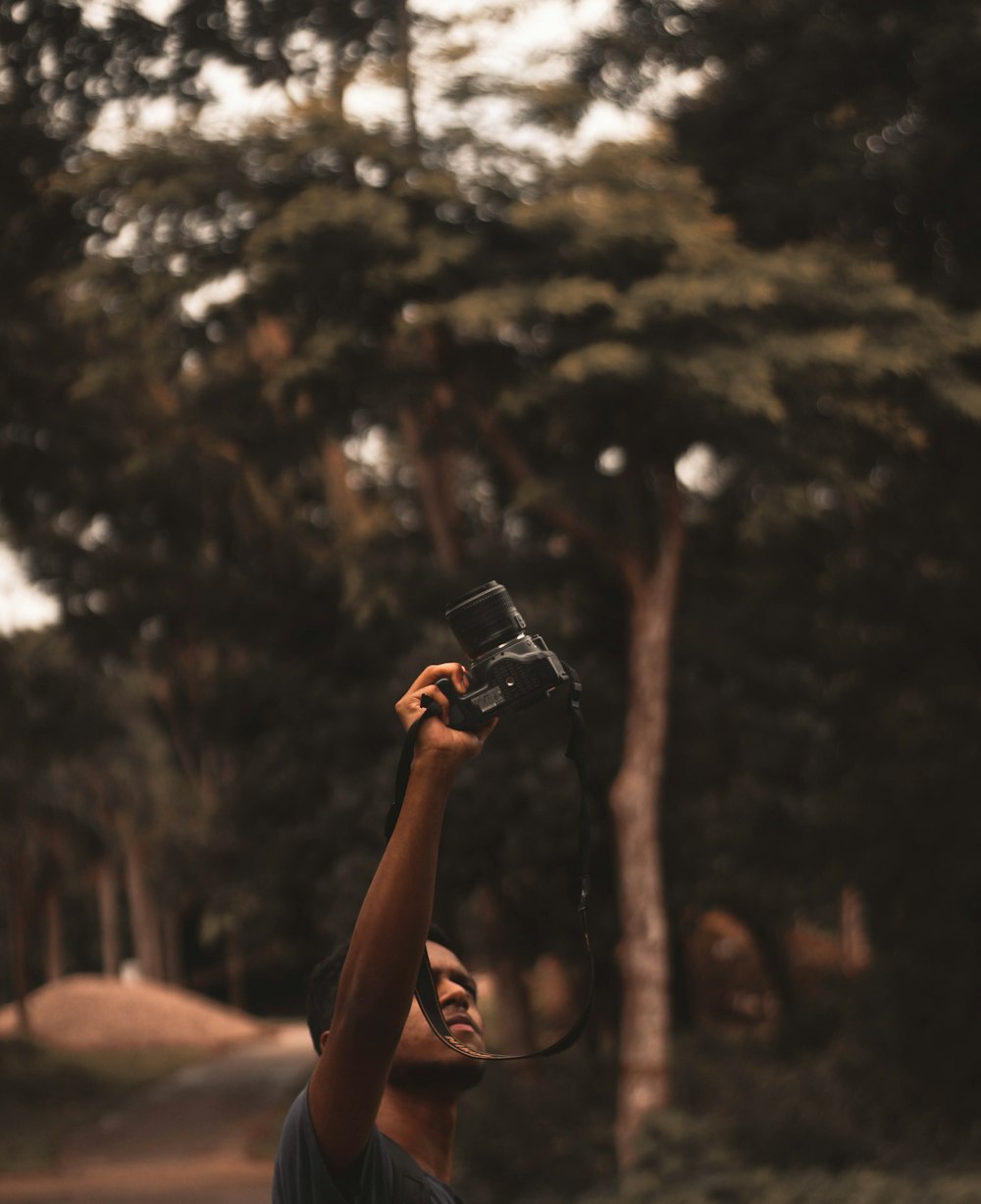 Persona che tiene lo smartphone nero che scatta foto degli alberi durante il giorno