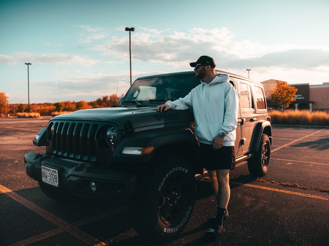 man in white shirt standing beside black jeep wrangler