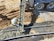 A construction worker is pouring concrete from a cement truck into a mold on a construction site. The area is surrounded by dirt and gravel, and the worker is wearing a high-vis vest and hard hat.