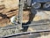 A construction worker is pouring concrete from a cement truck into a mold on a construction site. The area is surrounded by dirt and gravel, and the worker is wearing a high-vis vest and hard hat.