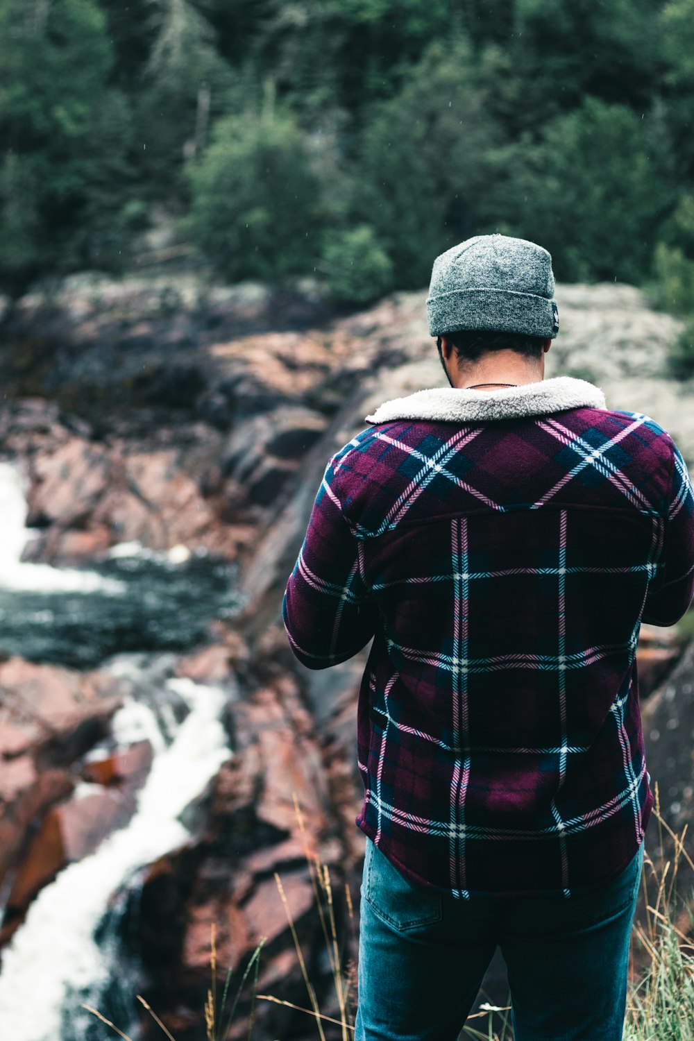 man in red and black plaid dress shirt and gray knit cap standing near green trees