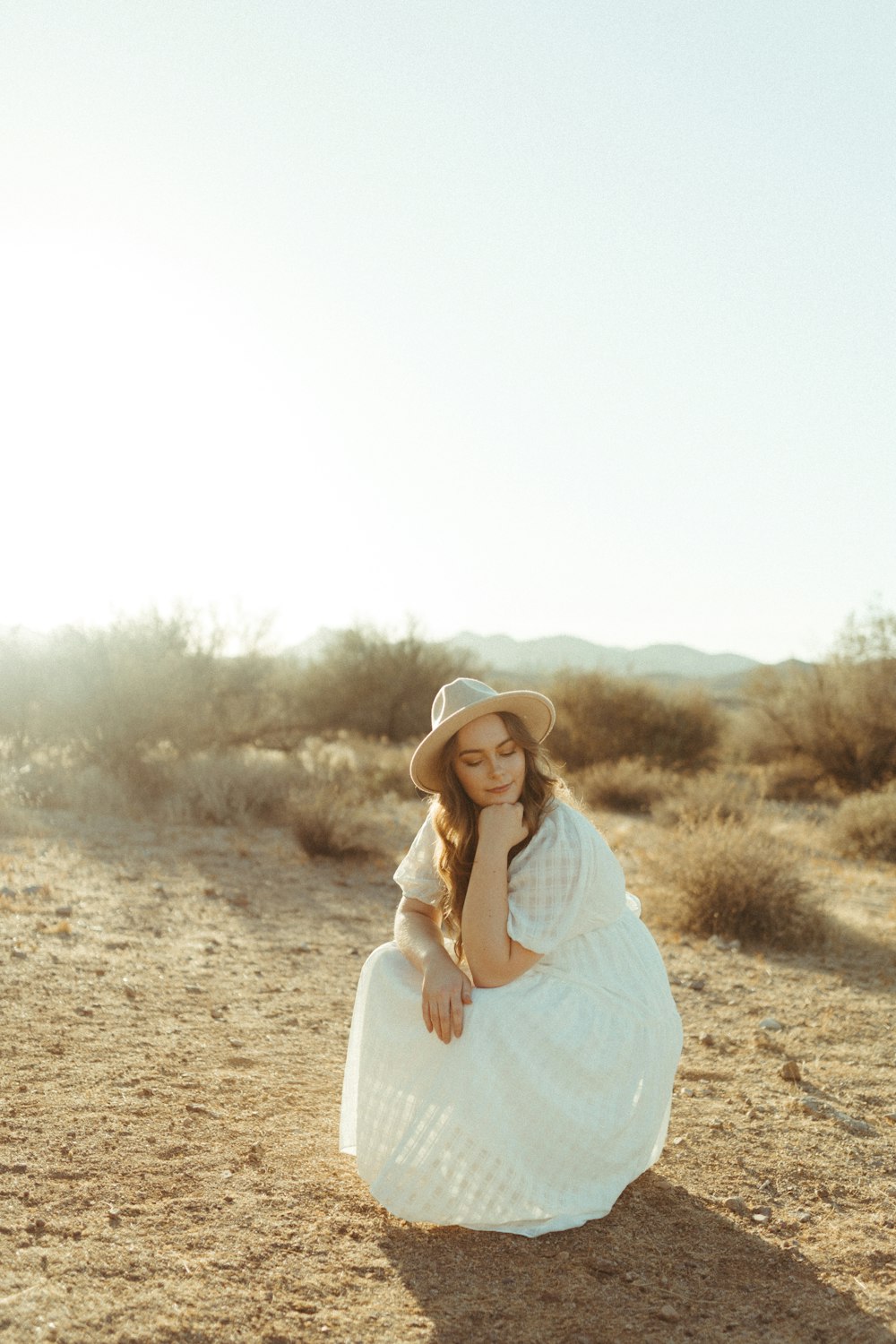 Mujer en vestido blanco de manga larga de pie en campo marrón durante el día