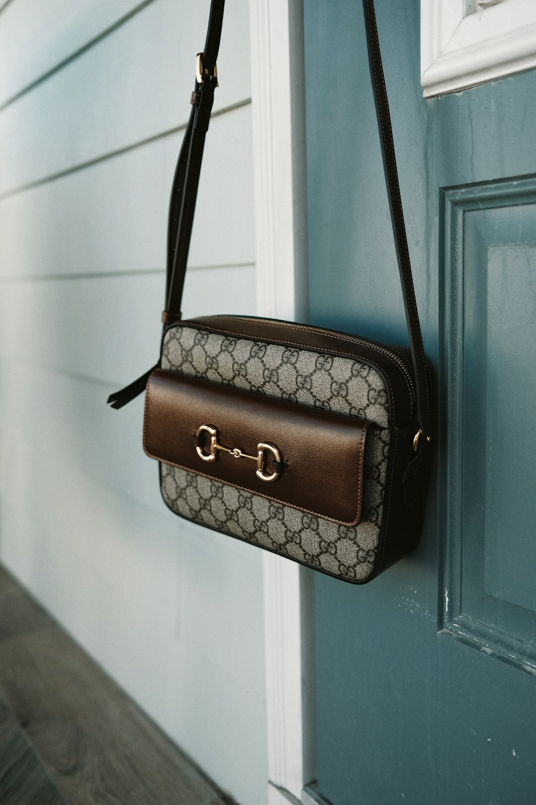 brown leather sling bag hanging on white wooden door