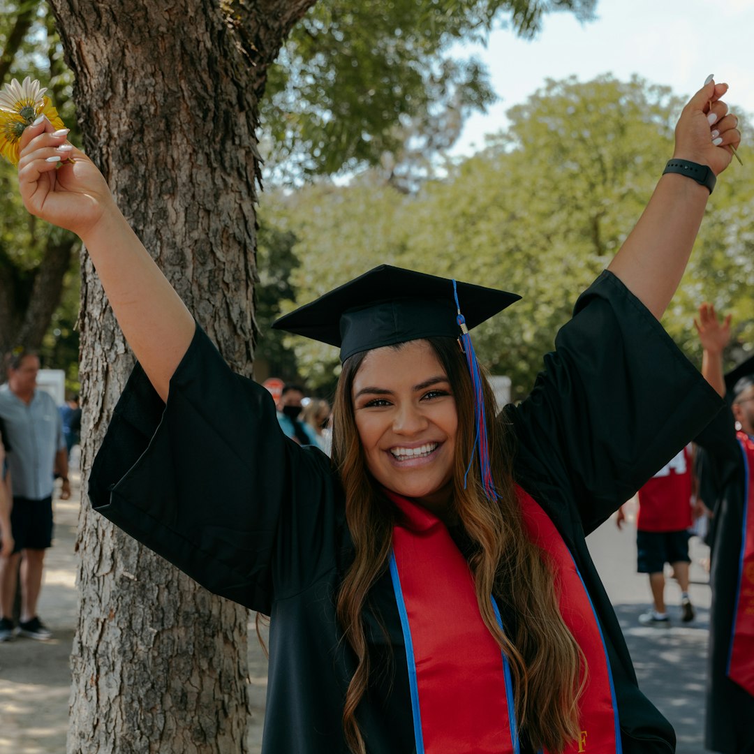 woman in academic dress and academic hat standing beside tree during daytime