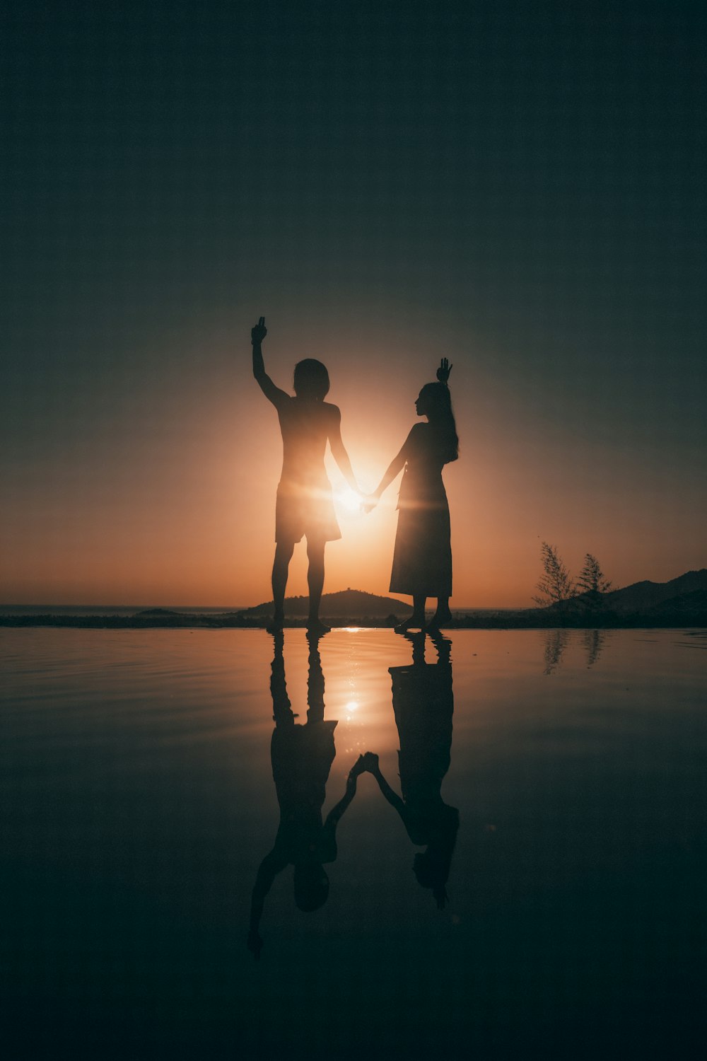 silhouette of 2 person standing on seashore during sunset