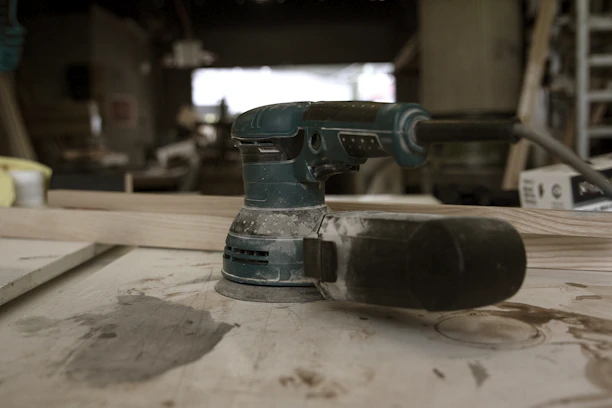 Close-up of a rugged power drill resting on a worn wooden workbench in a busy workshop.