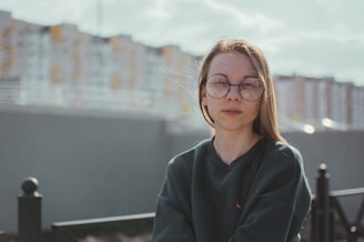 Person wearing Lunnec glasses outdoors, with a cityscape softly blurred in the background.