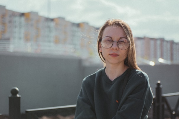 Person wearing Lunnec glasses outdoors, with a cityscape softly blurred in the background.