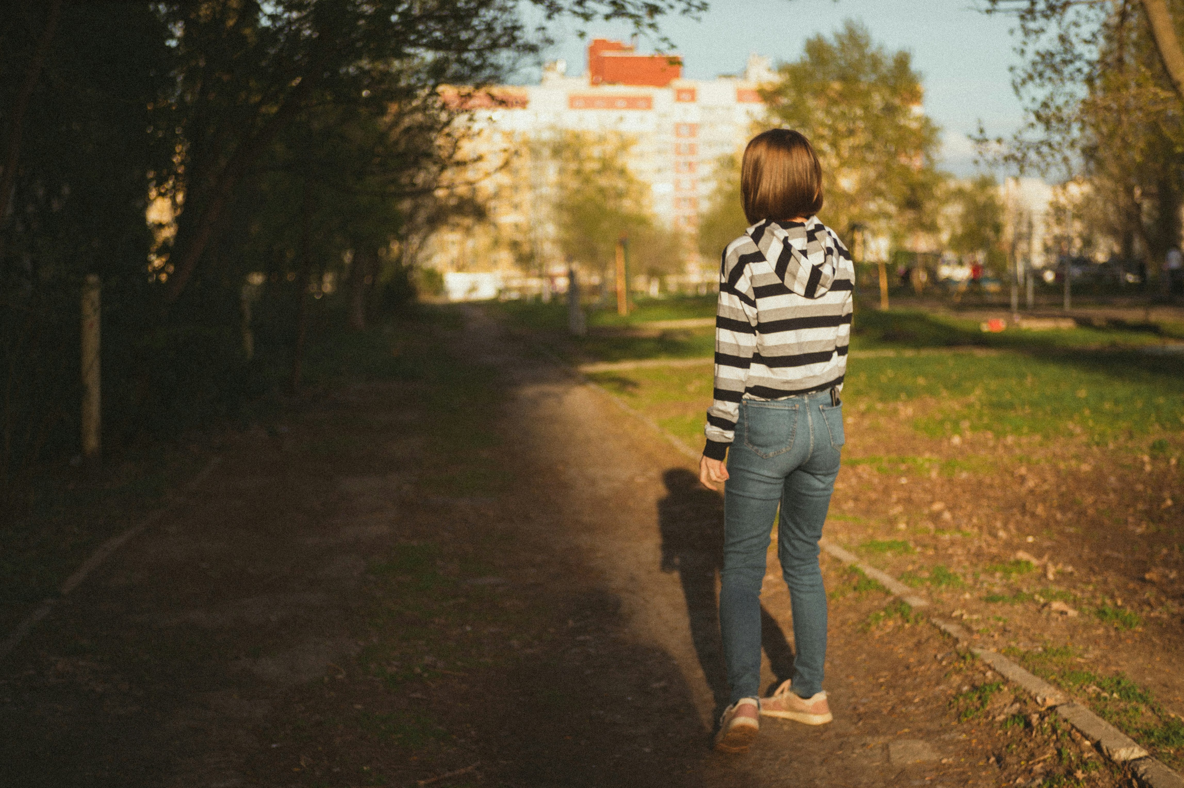 girl in white and black striped long sleeve shirt and blue denim jeans standing on pathway