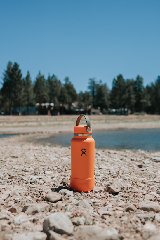 Orange Hydroflask, next to a lake.