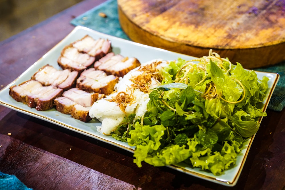 sliced meat with green vegetable on brown wooden tray
