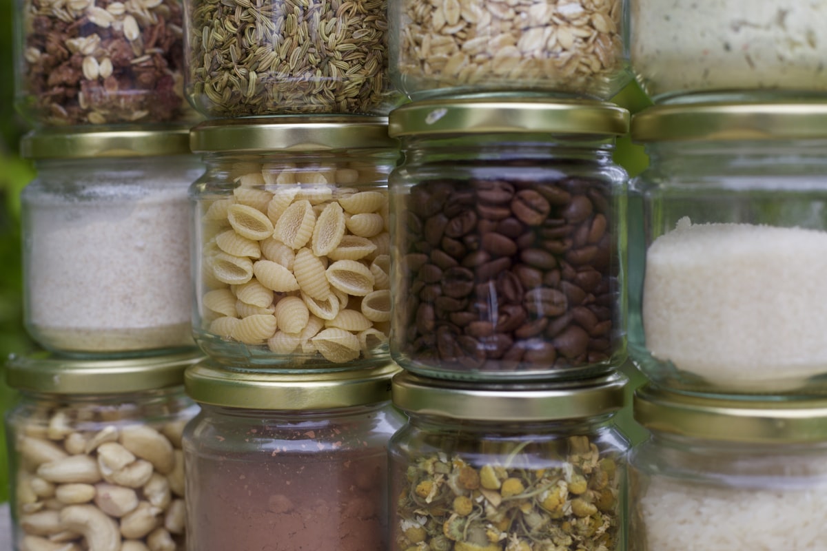 Stacked clear glass pantry jars with metal screw-on lids filled with nuts and grains