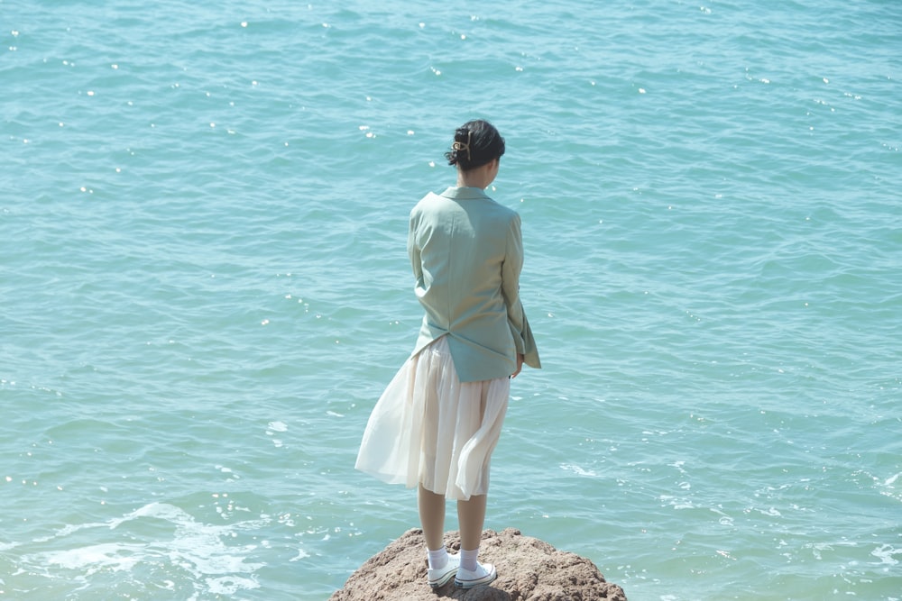 woman in white dress standing on rock near body of water during daytime