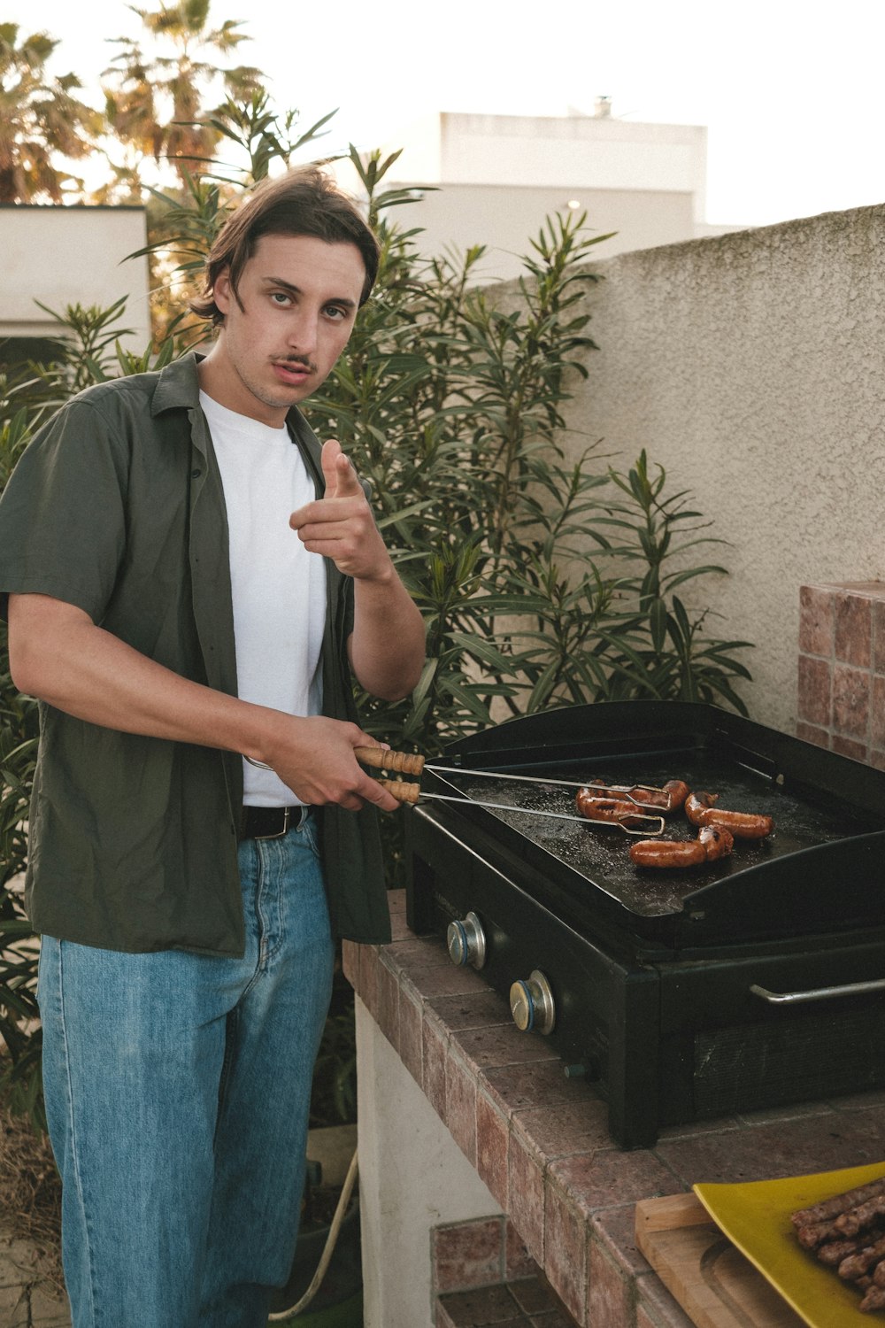 man in black crew neck t-shirt and blue denim jeans holding black frying pan