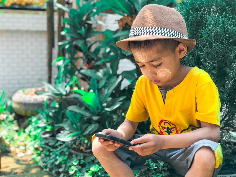 boy in yellow crew neck t-shirt and brown hat sitting on ground