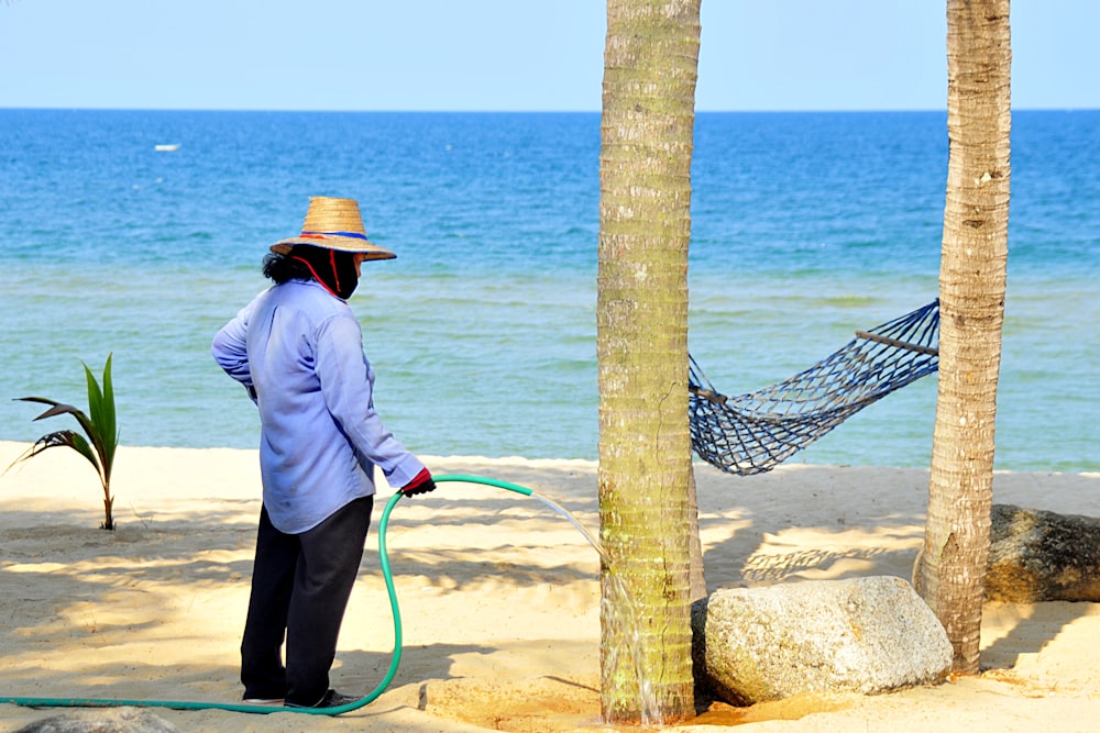 man in white dress shirt and brown hat standing on brown rock near sea during daytime