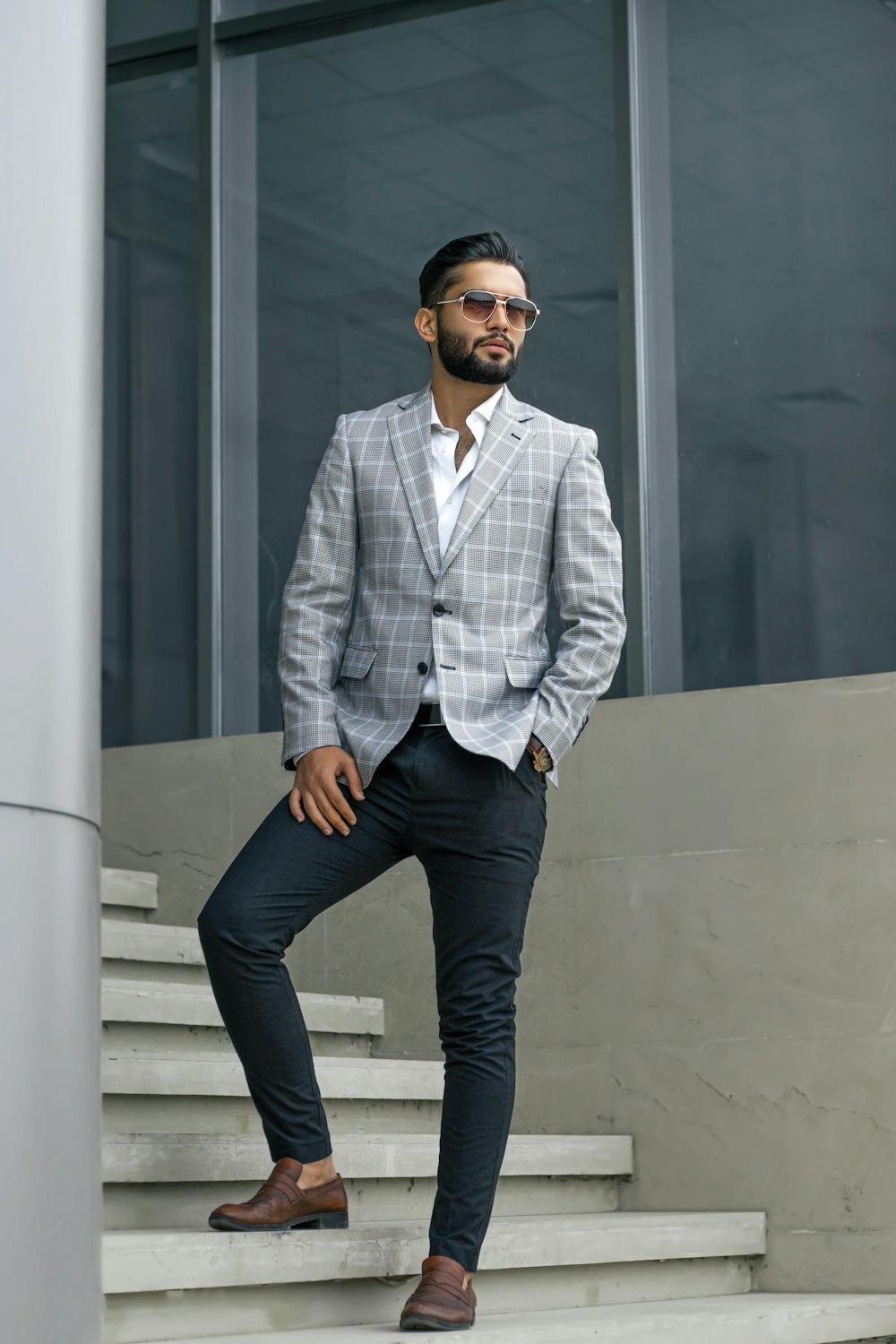 man in blue and white pinstripe dress shirt and blue denim jeans standing beside white wall