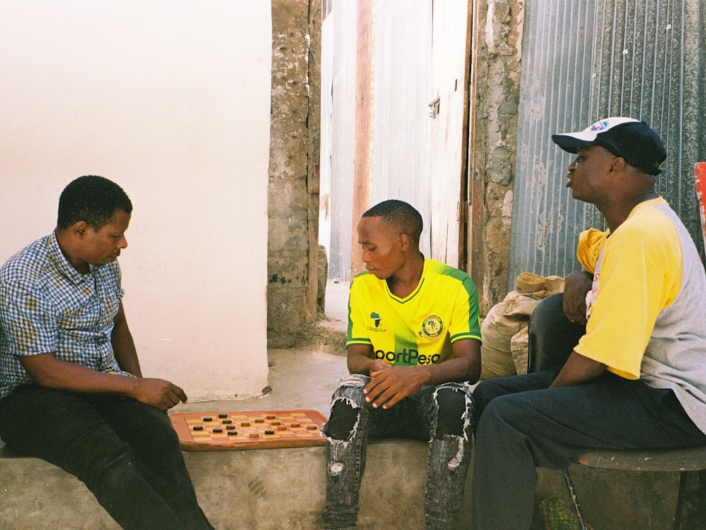 man in yellow crew neck t-shirt sitting beside man in blue and white checkered button