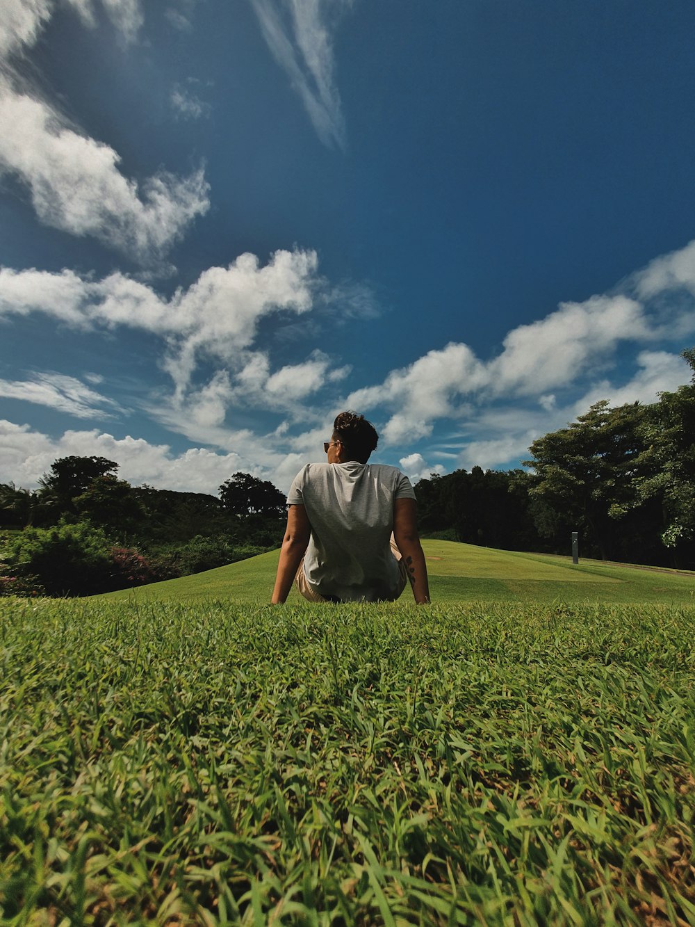 man in white t-shirt sitting on green grass field under blue and white cloudy sky