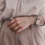 Woman wearing layered bracelets and a stylish watch, hands resting on a wooden table.