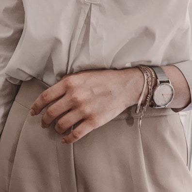 Woman wearing layered bracelets and a stylish watch, hands resting on a wooden table.