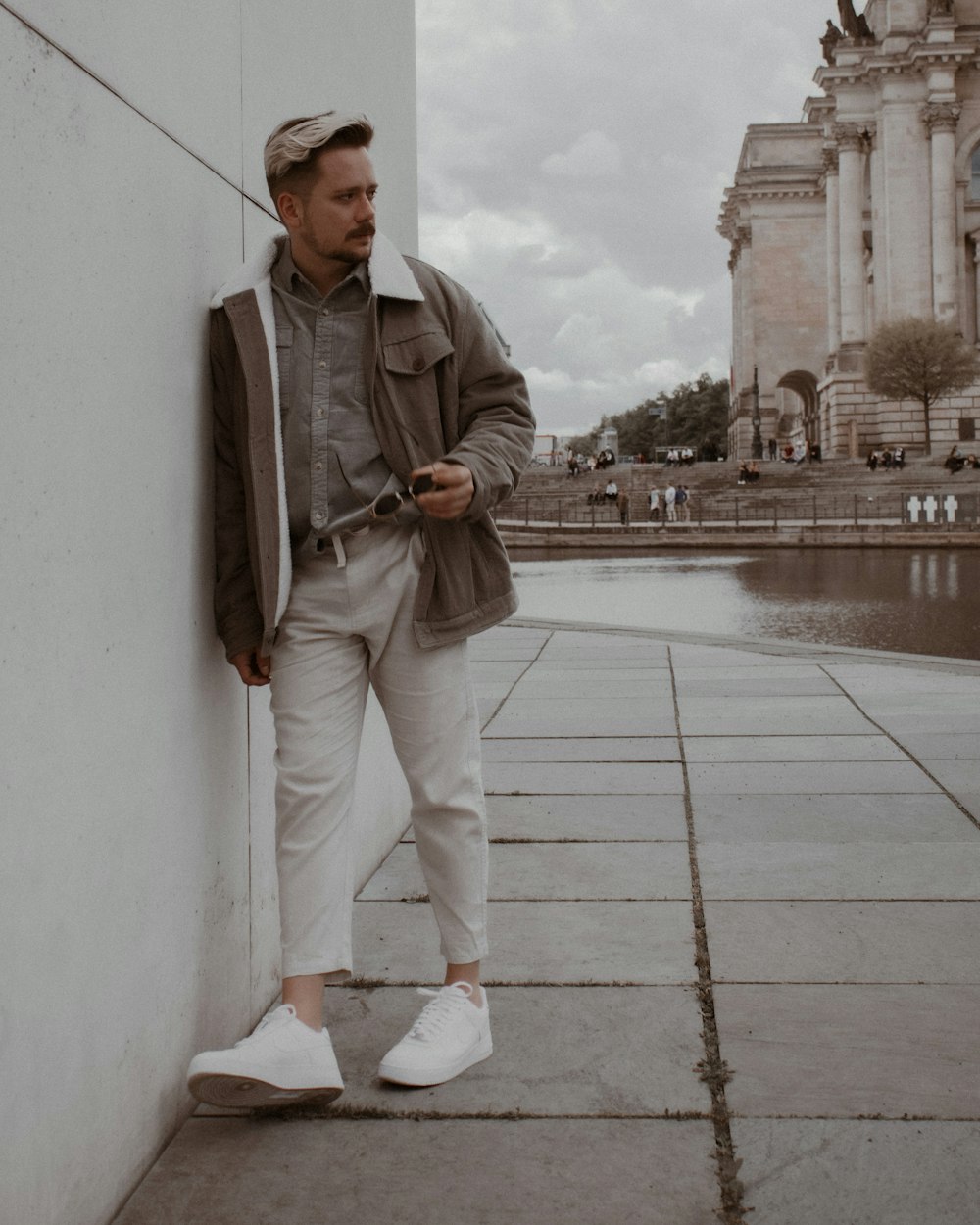 man in gray zip up jacket and white pants standing on gray concrete floor during daytime