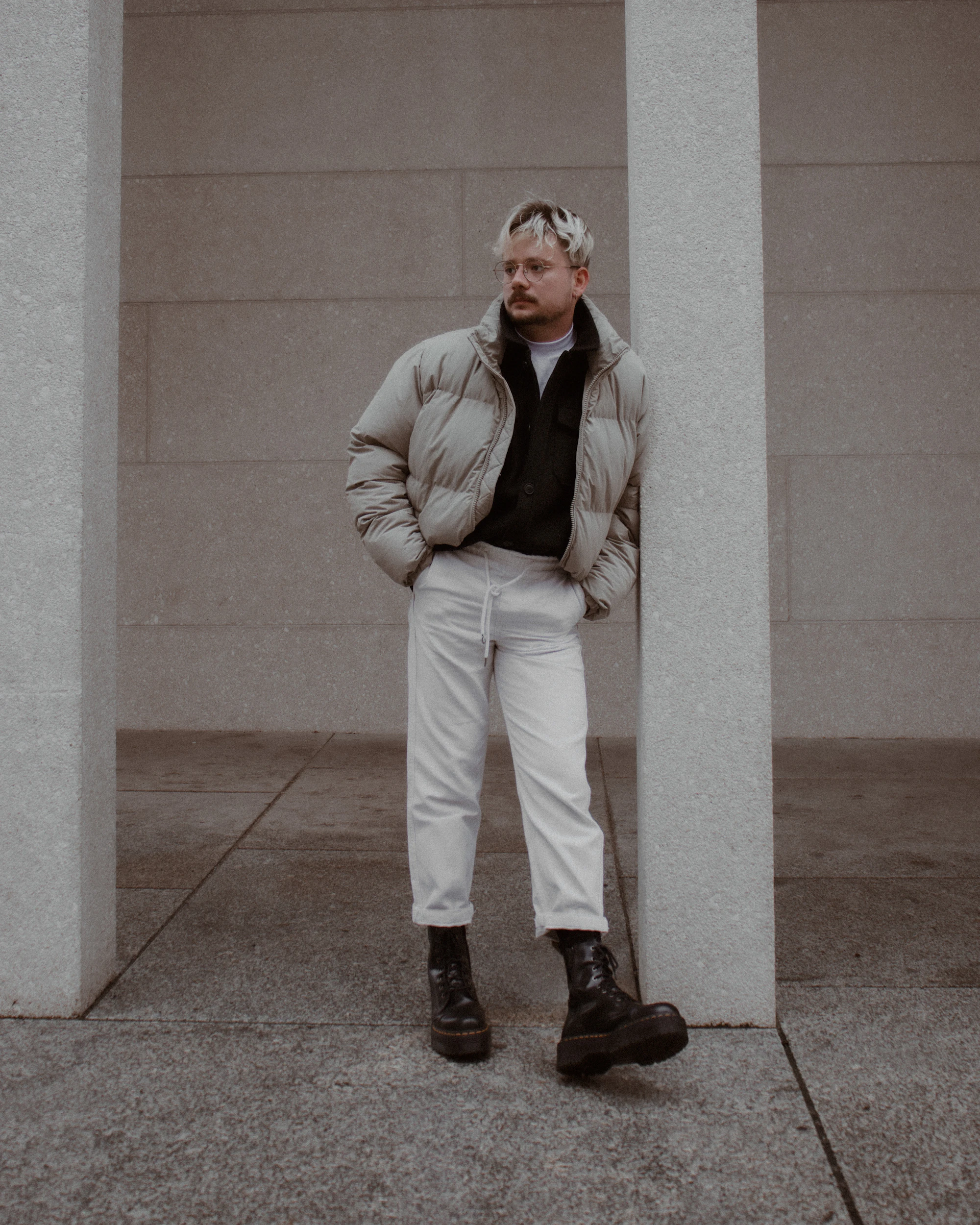 A man in a grey jacket by a concrete wall