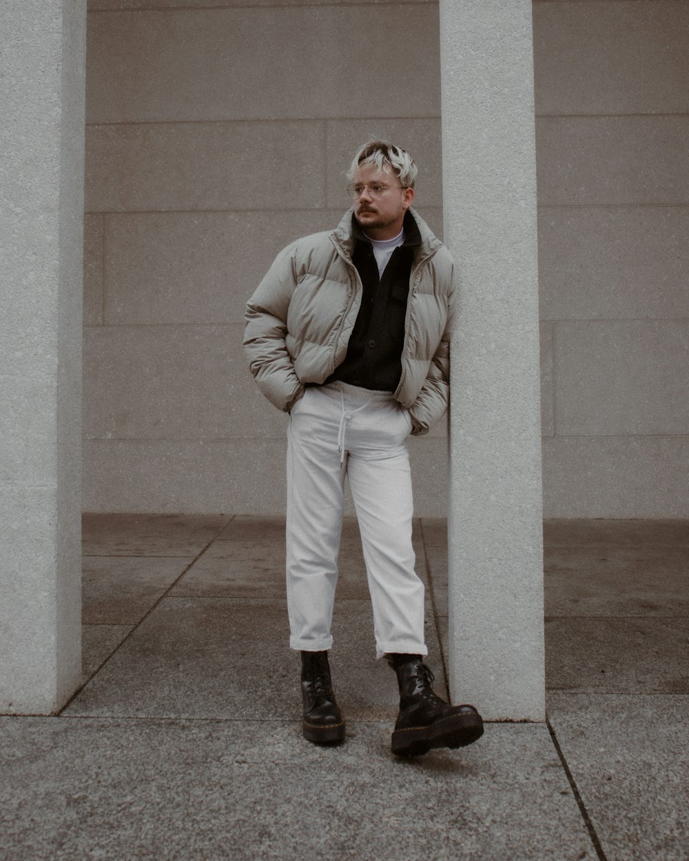 man in gray suit jacket and white pants standing beside white concrete wall