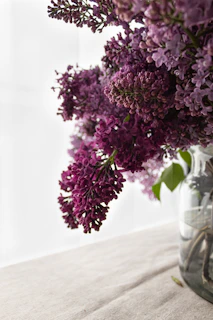 Close-up of a delicate bouquet blending soft lilacs and deep purples, styled with natural greenery on a white marble surface.