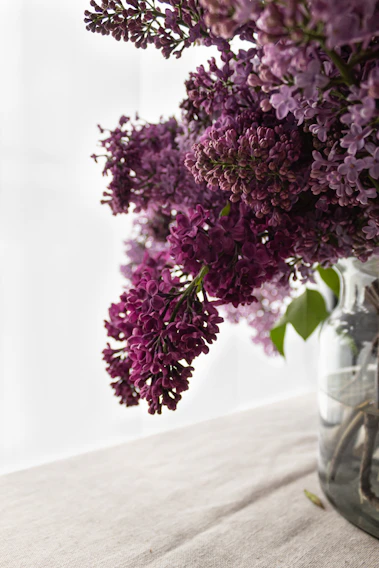 Close-up of a delicate bouquet blending soft lilacs and deep purples, styled with natural greenery on a white marble surface.