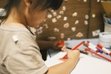 Close-up of a child's hand sketching AI ideas in a notebook with colorful markers.