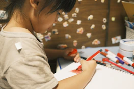 A close-up of a child's hands sketching ideas in a notebook, surrounded by study materials.
