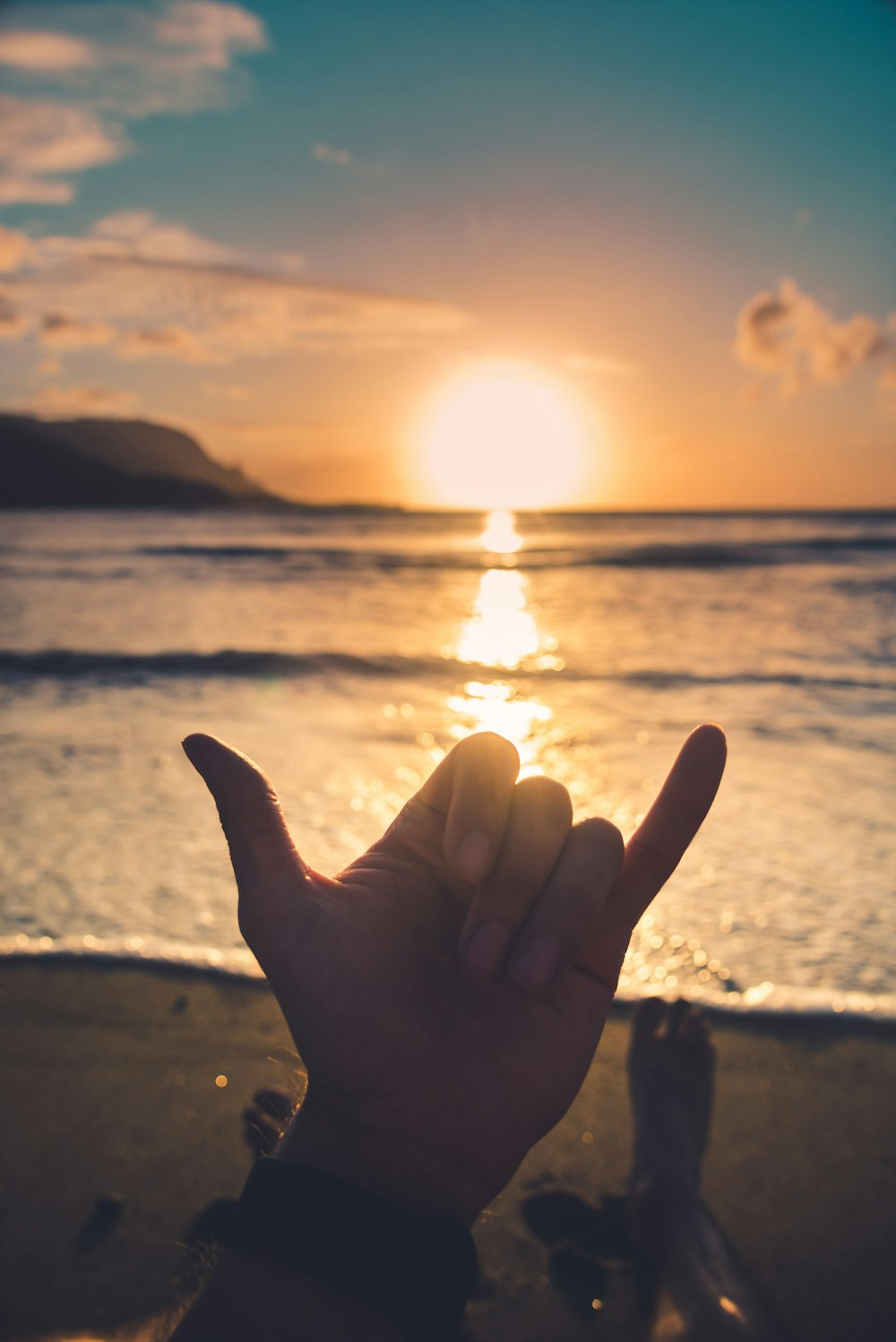 person doing peace sign near sea during sunset