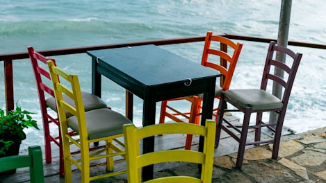 A vibrant colorful dining chair set around a rustic wooden table.