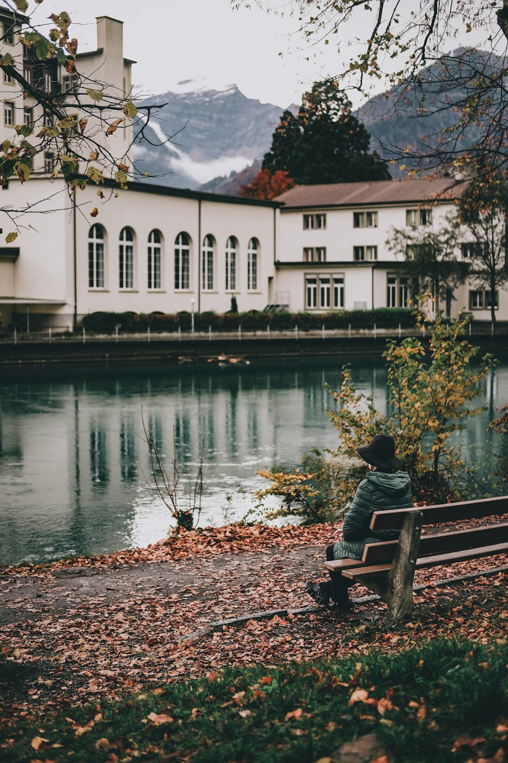 man in black jacket sitting on bench near river during daytime