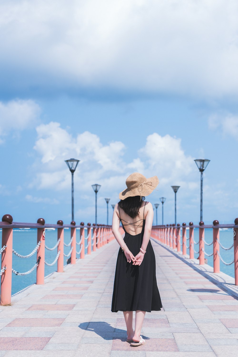 mulher no vestido preto que usa o chapéu do sol marrom em pé na doca de madeira durante o dia