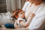 A close-up image of a mother breastfeeding her baby. The child is wearing a striped shirt, and the scene conveys a sense of intimacy and nurturing. Soft lighting and neutral tones create a warm atmosphere.