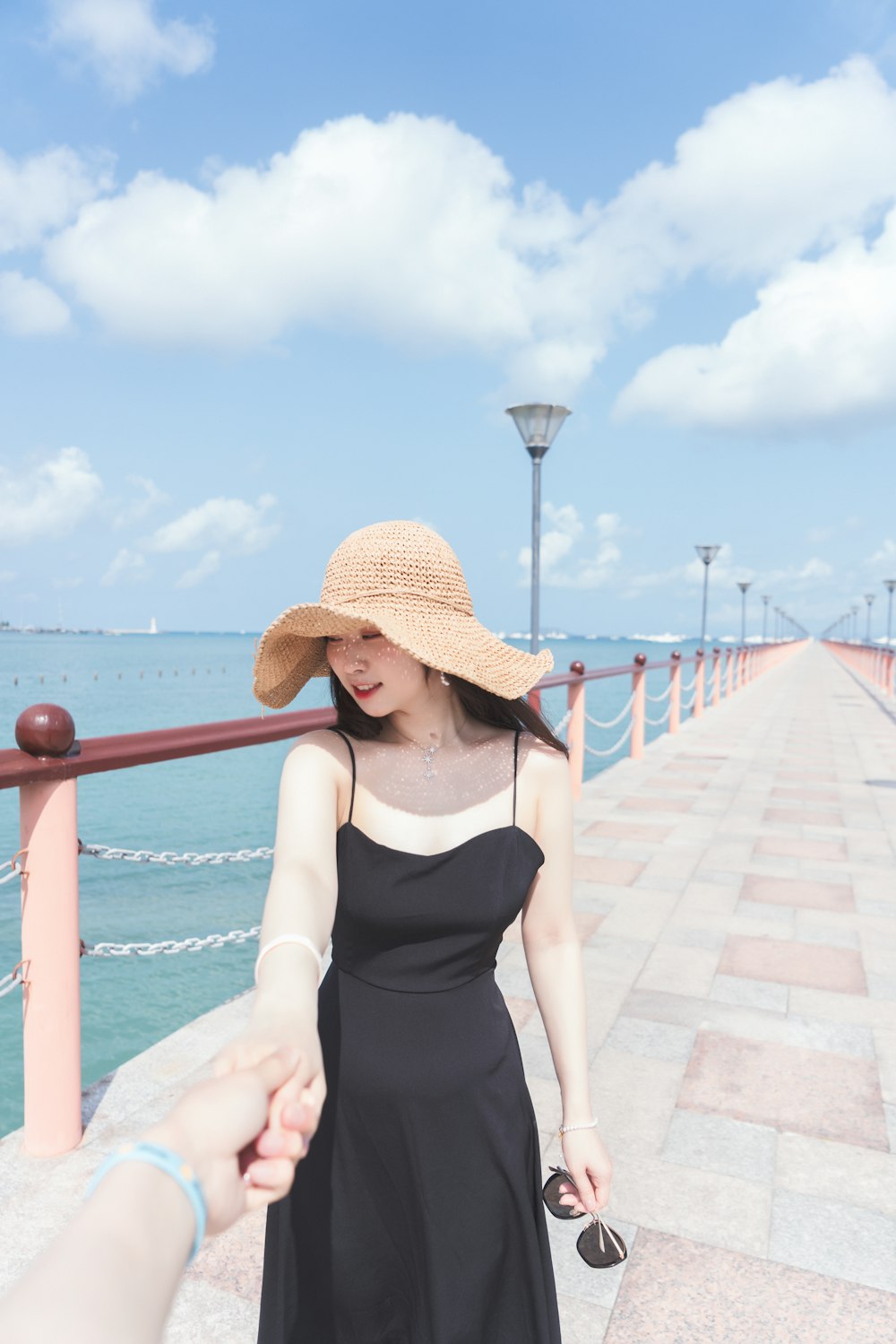 Femme en débardeur noir portant un chapeau de soleil marron debout à côté de balustrades en métal rouge pendant la journée