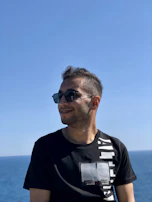 A person wearing classic aviator sunglasses, smiling under a clear sunny sky.