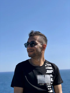 A person wearing classic aviator sunglasses, smiling under a clear sunny sky.