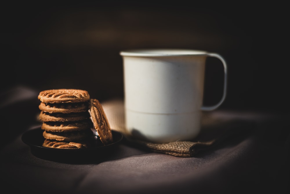 white ceramic mug beside brown cookies on black textile