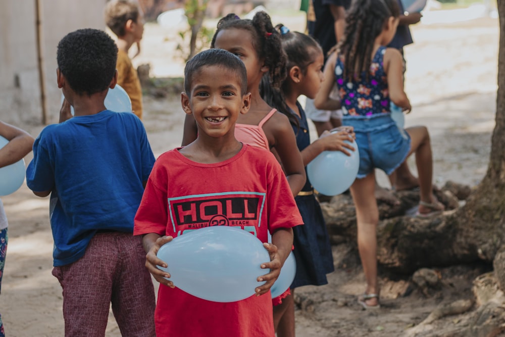 menino na camiseta vermelha do pescoço da tripulação segurando a bola branca