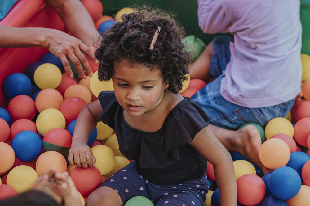 girl in black shirt and blue denim shorts sitting on yellow and pink balloons