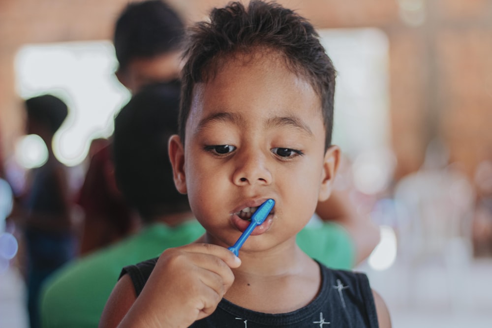 Niño con camisa negra de cuello redondo sosteniendo bolígrafo azul