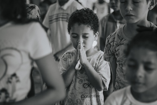 A quiet moment of prayer with children holding hands under a large tree.