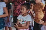 girl in white and red crew neck t-shirt standing near people during daytime