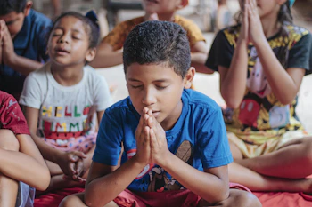 Children participating in a group meditation session under the shade of trees.