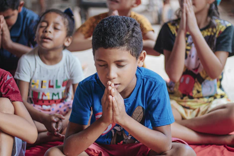Children sitting cross-legged on soft mats in a pastel-colored yoga studio, smiling gently during a calm breathing exercise.