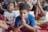 A group of children sitting cross-legged with their eyes closed and hands pressed together in a prayer-like position. The children are wearing colorful clothes and appear to be in a calm and focused state.
