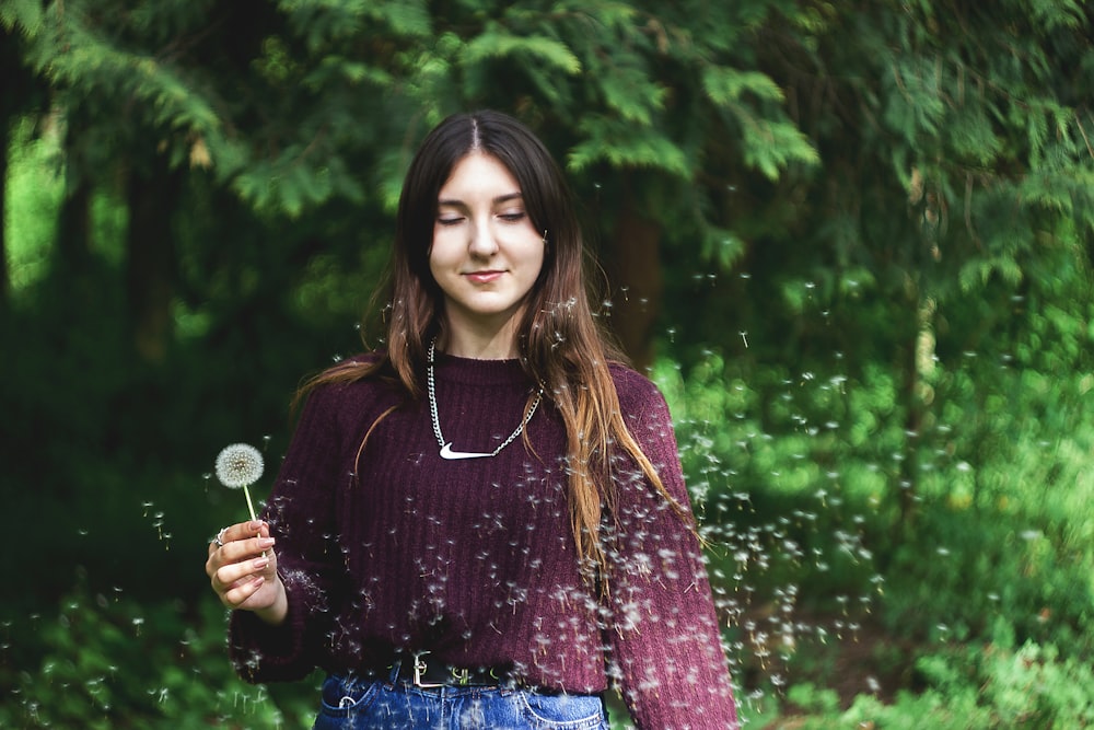 woman in purple and brown long sleeve shirt holding white dandelion flower during daytime